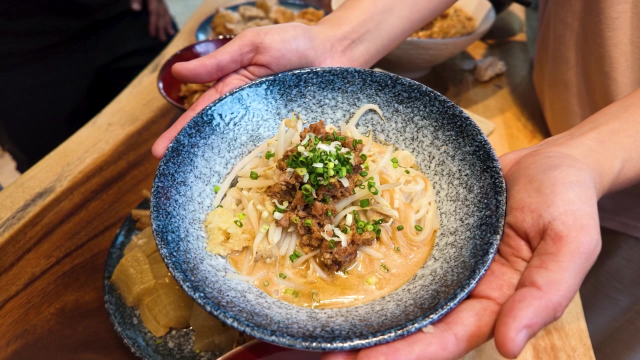 Mani che tengono una ciotola di Ma Jiang Mian con salsa di sesamo e carne di maiale macinata.