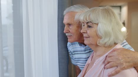 La-Pareja-De-Ancianos,-Abuelo-Y-Abuela,-Se-Abrazan,-Abrazan-Y-Miran-Por-La-Ventana