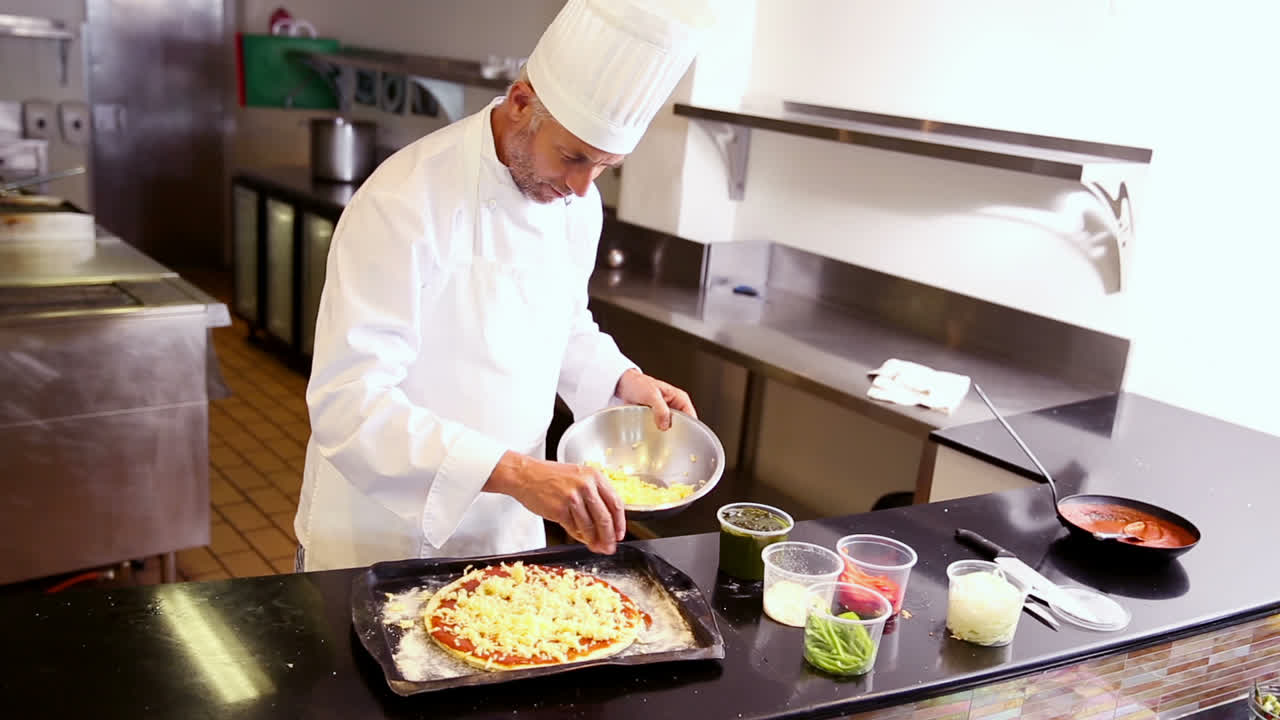 Cuoco unico che spruzza formaggio su una pizza