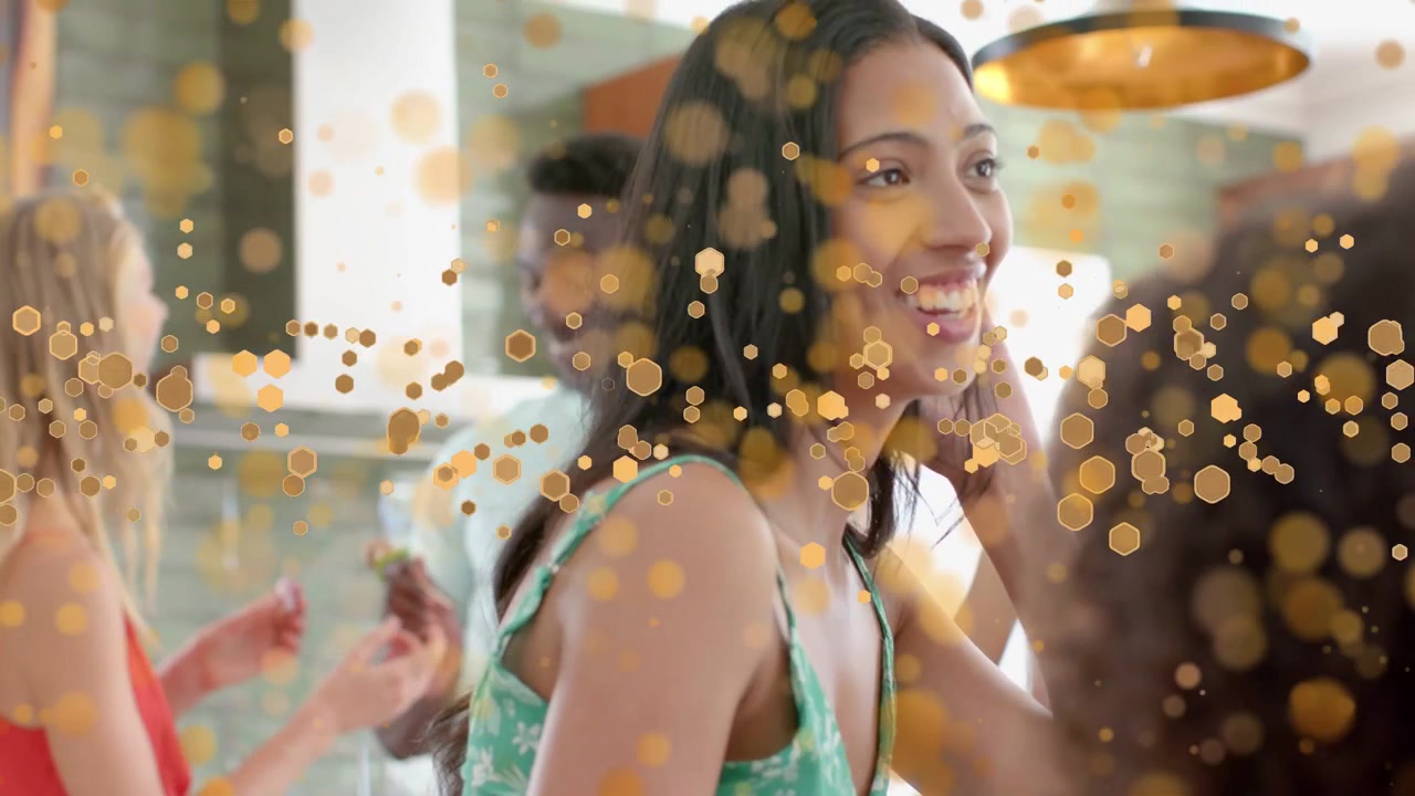 Donna che reagisce a un'amica fuori campo in cucina, sorridendo e toccandosi i capelli, con sovrapposizione di bokeh dorato.