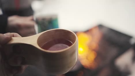 man holding a wooden cup with hot beverage in winter forest in lemmenlaakso, finland