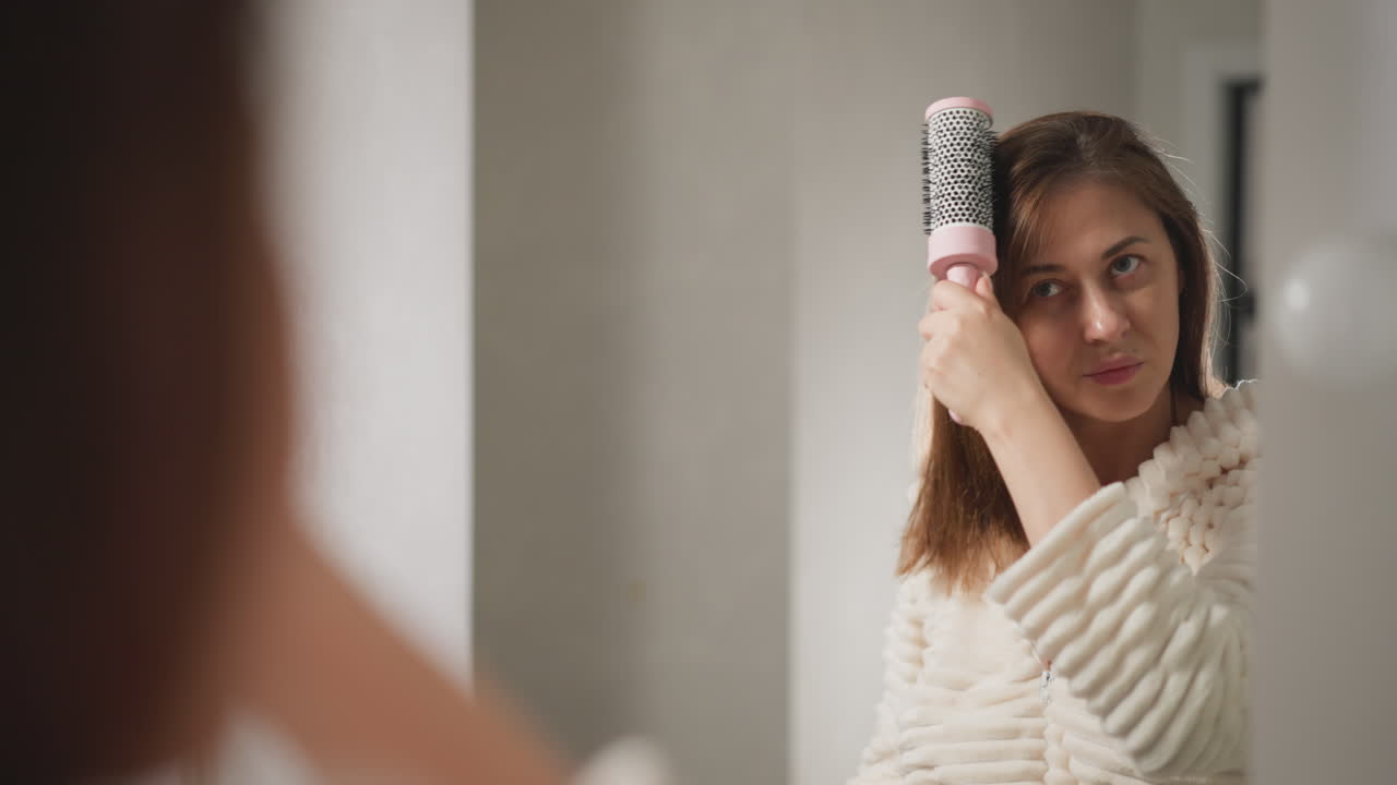 mujer combina el cabello con el cepillo después de tomar una ducha en el baño. mujer endereza el cabello mojado con un peine en el baño contemporáneo con lámparas en cámara lenta