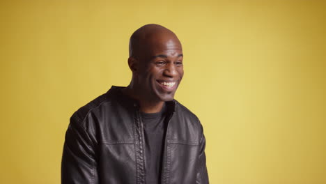 head and shoulders studio portrait of smiling and laughing mature man against yellow background 8