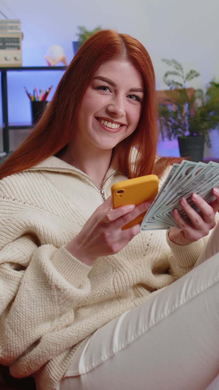 Smiling happy young woman counting money cash use smartphone income saves lottery win budget at home