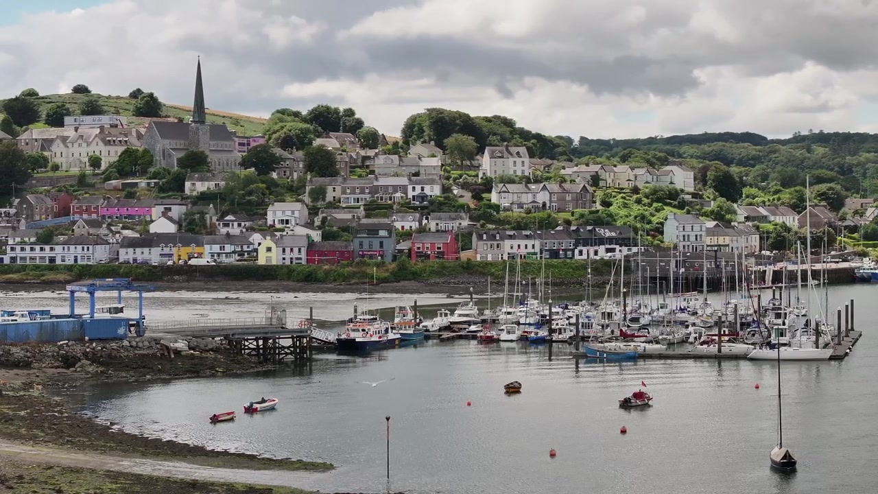 Una ripresa panoramica con drone che cattura le case colorate, il campanile della chiesa e il porto turistico per barche a vela di Crosshaven, Irlanda. Perfetto per documentari di viaggio e contenuti sul turismo europeo.