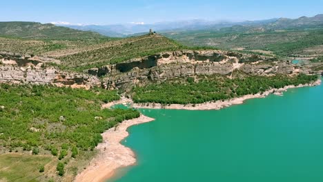 Cabeza-De-Roca-De-La-Montaña-Española-Con-El-Agua-Fluye-Sobre-Su-Pie,-Cubierta-De-Vegetación-Verde,-Lago-De-Agua-Azul