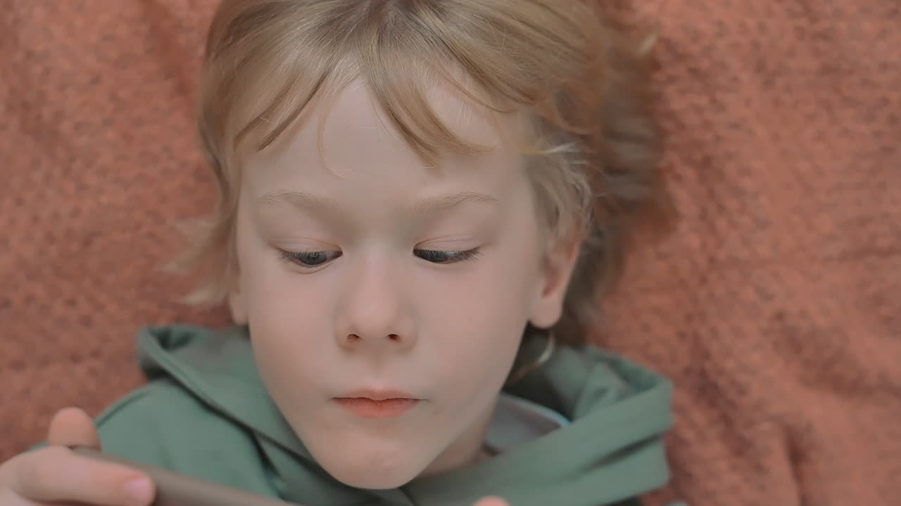 Portrét malého chlapce s chytrým telefonem sledujícího film.