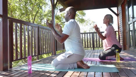 focused senior african american couple practicing yoga on mats on sunny terrace, slow motion