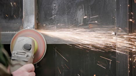 limpieza manual caucásica de costuras soldadas con una molienda angular con un disco de flap en la construcción metálica soldada de primer plano con largos rastros de chispas, cámara lenta