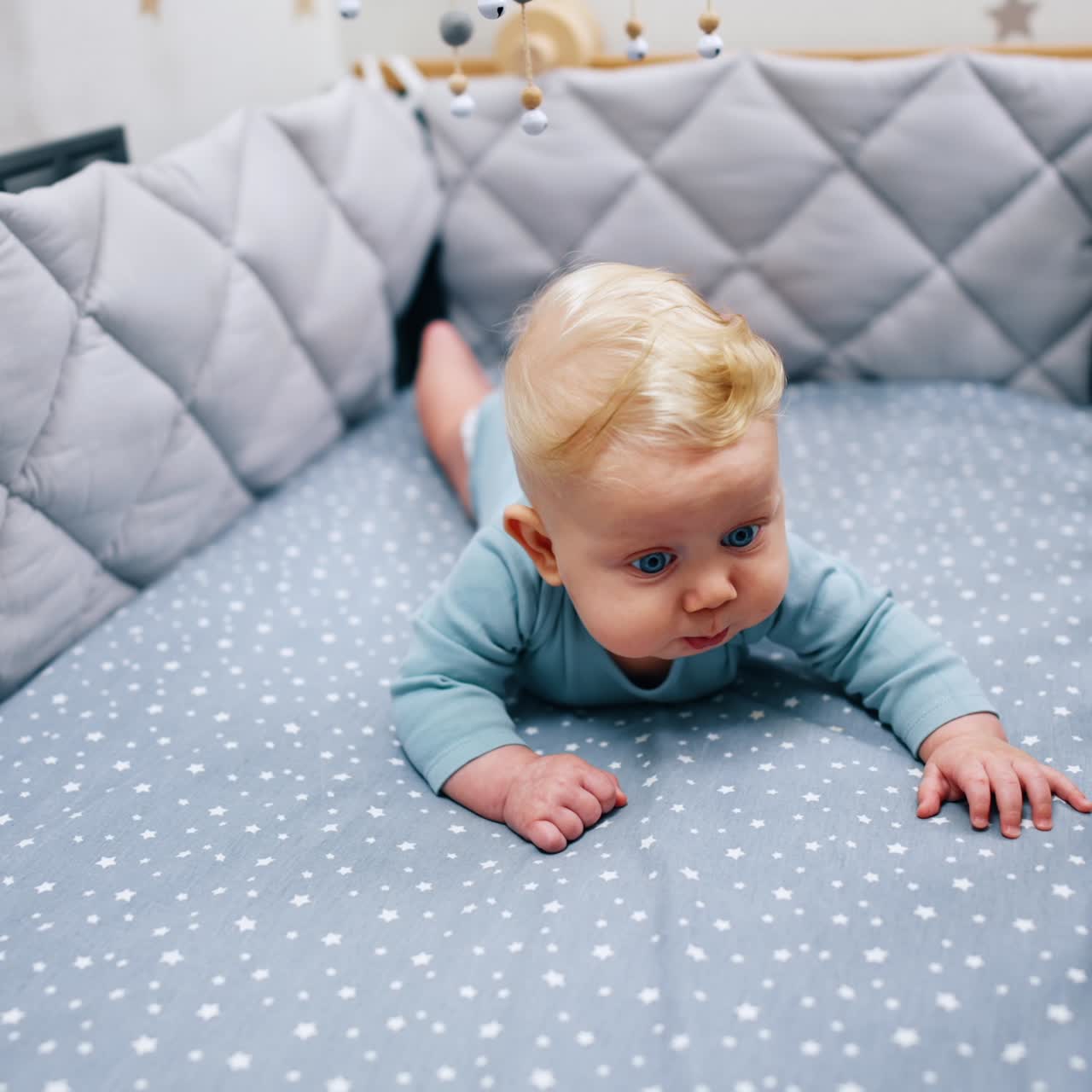 Adorabile bambino sdraiato a pancia in giù nella culla blu. Una giostrina pende sopra il bambino.