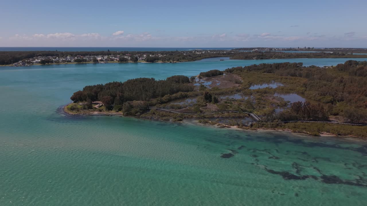 Clear turquoise ocean surrounds Pirrita Island, peaceful mid-morning light and natural beach tones, aerial establishing