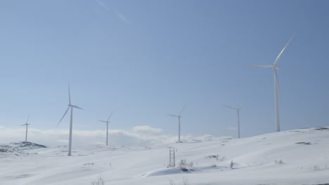 camera pans down to reveal a vast field of wind turbines spinning in a snow-covered alpine mountain setting. captures the scale of renewable power in remote, sunlit wilderness terrain.