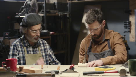 old father carpenter teaching his young son to process and work with timber in workshop