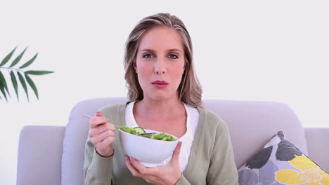 Content-blonde-woman-eating-salad-sitting-on-couch