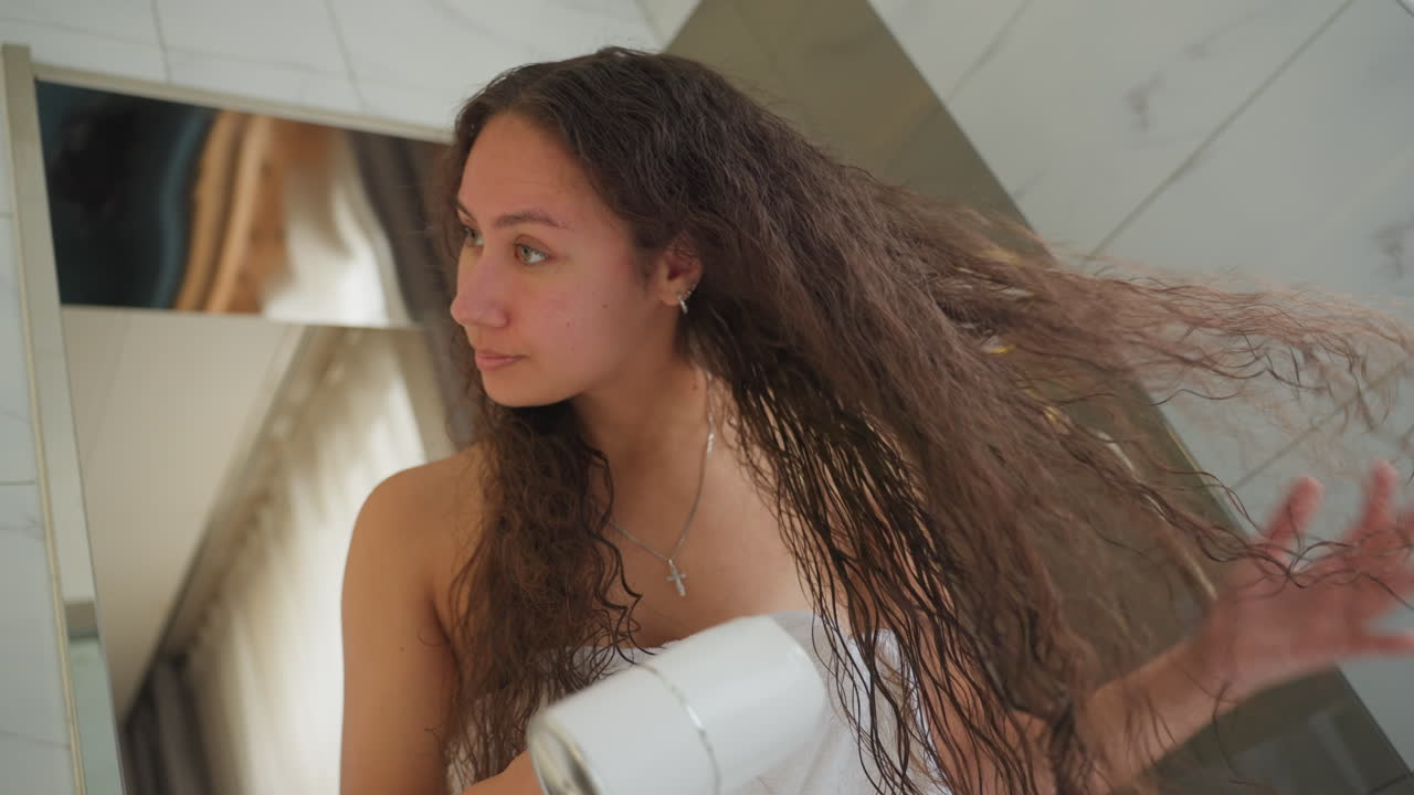 Ochtendschoonheidsvoorbereiding. Ochtendstylingsessie met vrouw die krullend haar droogt in het hotel. Vrouw droogt zorgvuldig haar spiraalkrullen tijdens haar ochtendverzorgingsroutine in de hotelbadkamer.