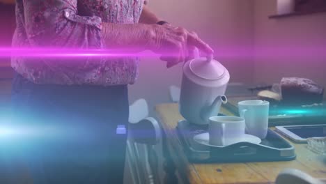 Animation-of-coloured-lights-moving-over-senior-woman-pouring-tea-at-home