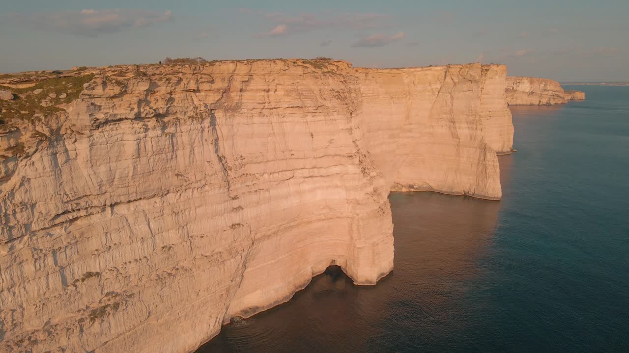 impresionantes acantilados de piedra caliza de malta se reflejan en el agua del mar mediterráneo a medida que el dron se acerca a la formación geológica