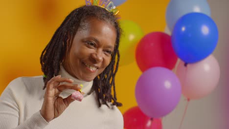 studio portrait of woman wearing birthday headband celebrating with balloons and party blower 1