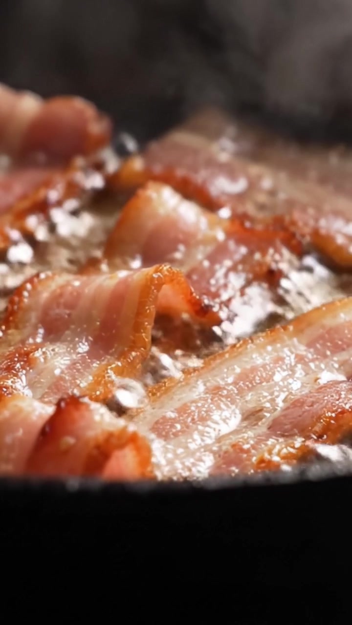 Sprød bacon: Et nærbillede af sprøde svinekødsstrimler, der steger i varm olie, og fanger den lækre aroma og gyldenbrune farve, mens de steger til perfektion.