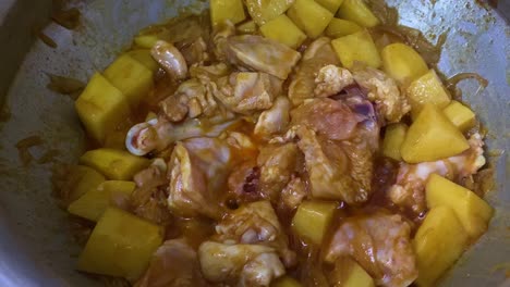 view of raw chicken being cooked with diced potatoes in metal pot