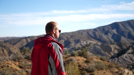 a young man in a red jacket camping in the california mountains on the edge of a cliff celebrating reaching his goal