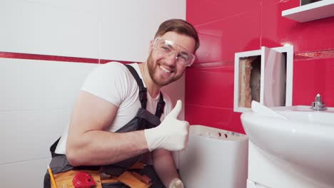 un fontanero profesional en el baño muestra su pulgar hacia arriba