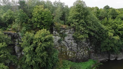 Aerial-View-of-Steep-Cliff-on-Rivers-Edge-With-Thick-Surrounded-by-Thick-Forestry