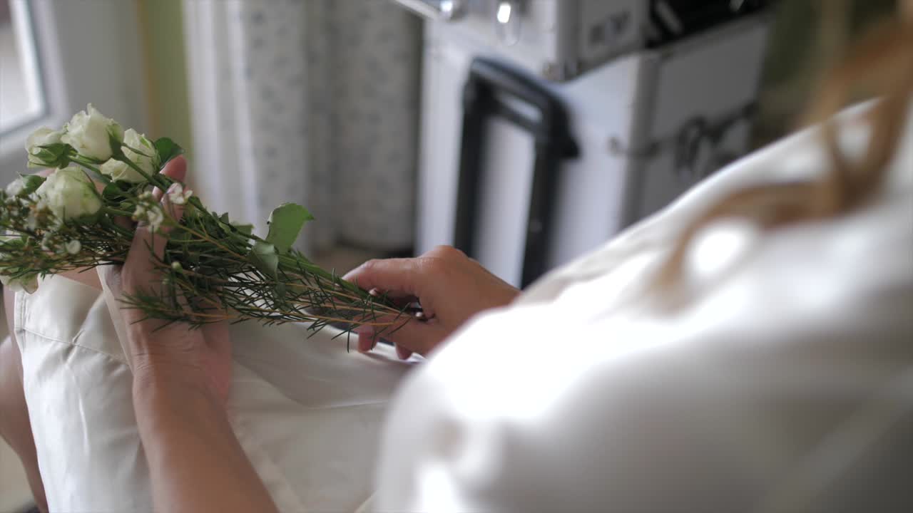 Woman dressed in morning robe holds wild flowers in her hands, sits near window