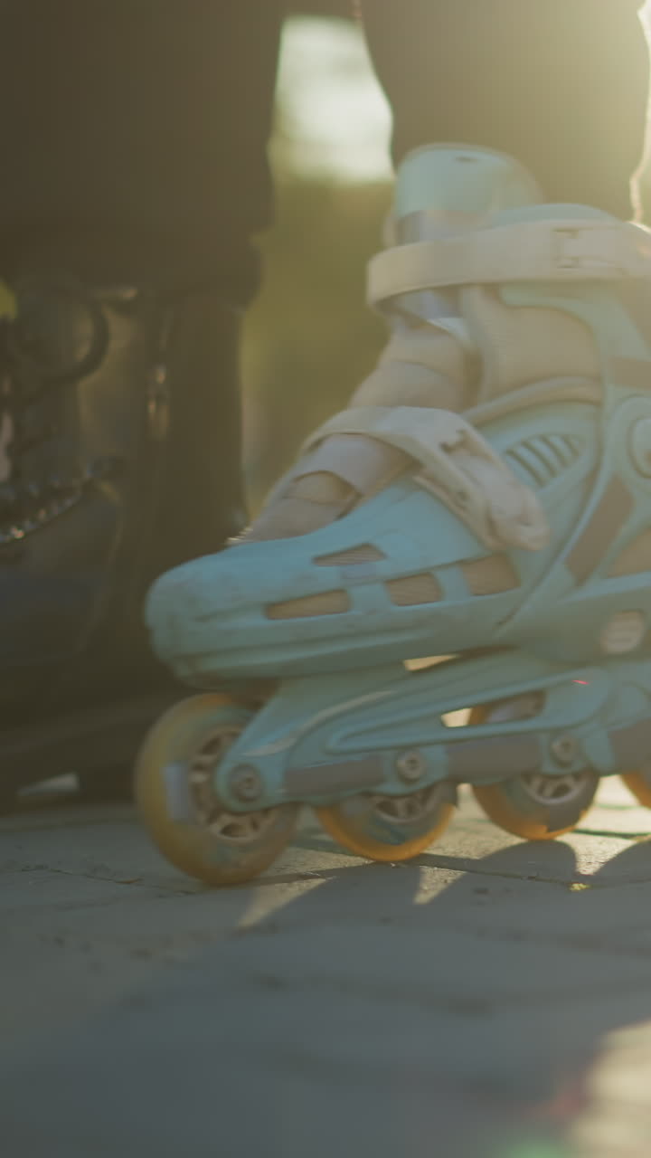A close-up shot of a person wearing a light blue rollerblade on one foot, with the rollerblade wheels in motion on a paved path in a park during a sunny day. The other foot is in a black boot