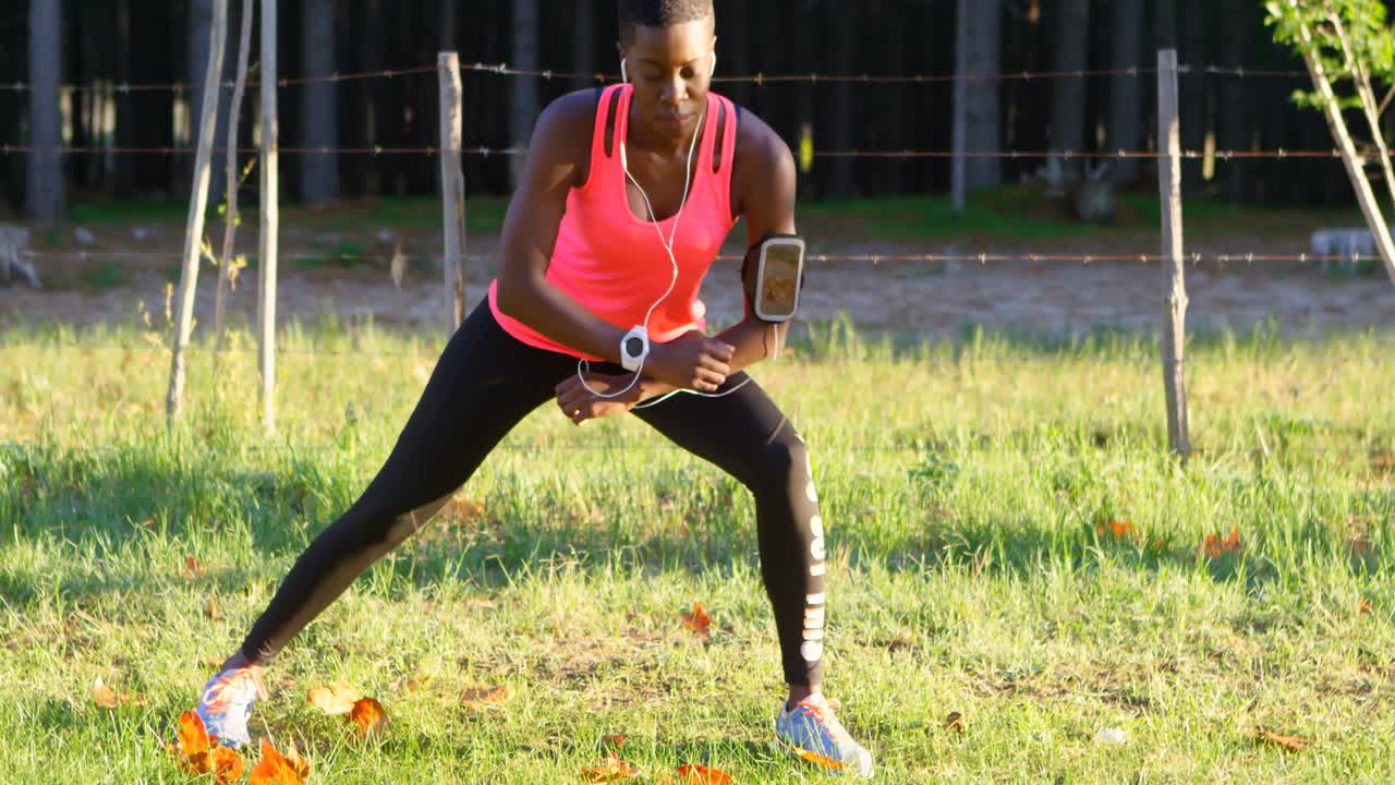 Female athlete performing stretching exercise while listening music in forest 4k