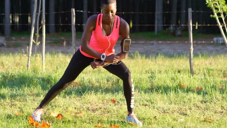 Female-athlete-performing-stretching-exercise-while-listening-music-in-forest-4k