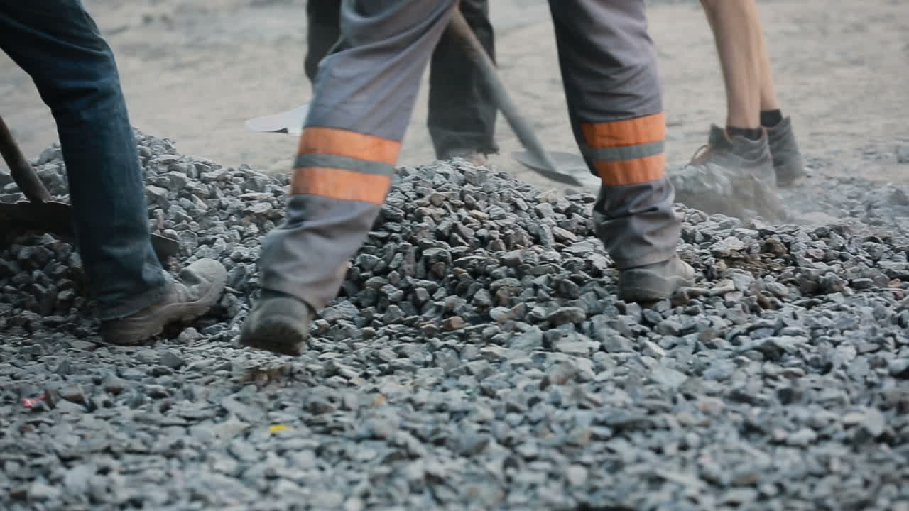 Workers team throw asphalt with shovels at road construction