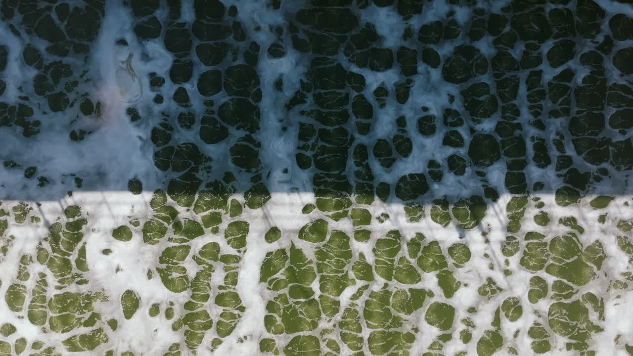 A detailed top-down image captures churning, frothy green water in an aeration basin, forming abstract bubble patterns
