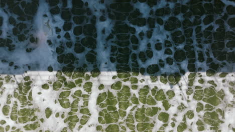 a detailed top-down image captures churning, frothy green water in an aeration basin, forming abstract bubble patterns