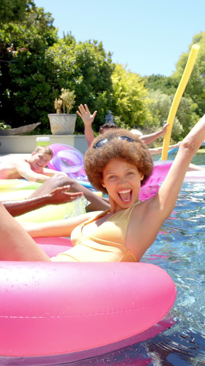 Vertical video of portrait of happy diverse friends playing with inflatables at pool party