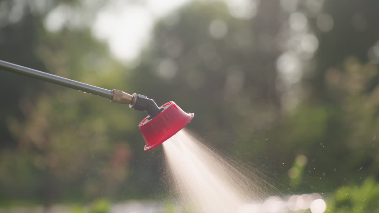 close up red nozzle spraying fine mist fumigation over green foliage in sunlit field conveying pest control process in protective agriculture setting with serene outdoor garden atmosphere