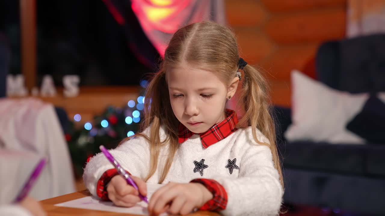 Portrait of a lovely little girl indoors at Christmas. Cute child writing a letter to Santa. Beautiful small girl drawing a picture on xmas background at home.
