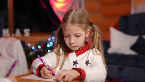 portrait of a lovely little girl indoors at christmas. cute child writing a letter to santa. beautiful small girl drawing a picture on xmas background at home.