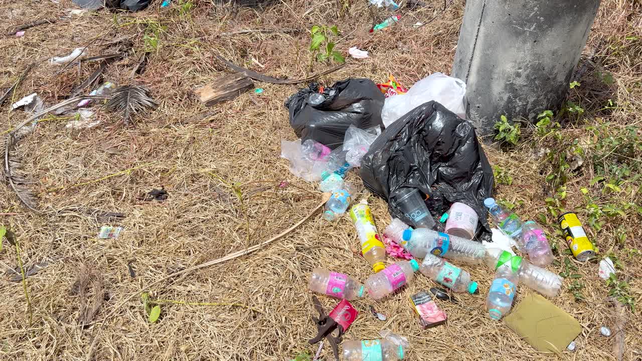 Inquadratura fissa dall'alto di bottiglie di plastica scartate e sacchi neri della spazzatura sull'erba secca.
