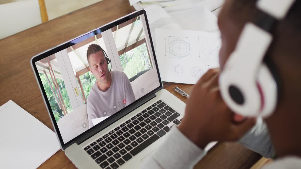 African american businessman sitting at desk using laptop having video call with male colleague