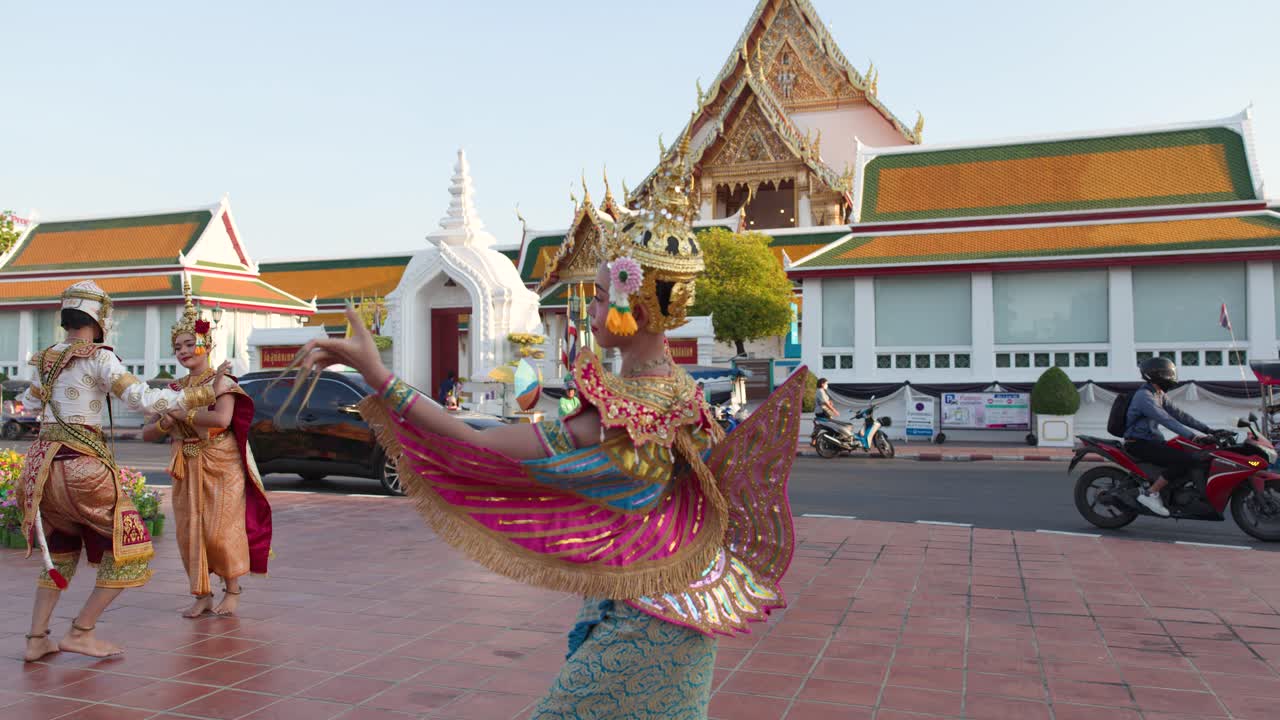 Danzatrici thailandesi in sontuosi costumi dorati eseguono movimenti classici Manohra all'esterno di un tempio storico di Bangkok.