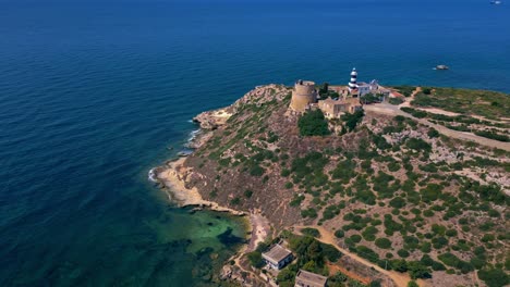 Standing-proud-on-rock-and-vegetation-covered-coastline,-Calamosca-Tower