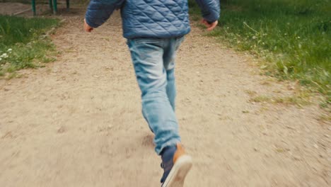 a boy, a child in jeans, sneakers and a quilted jacket runs on a gravel road in the park