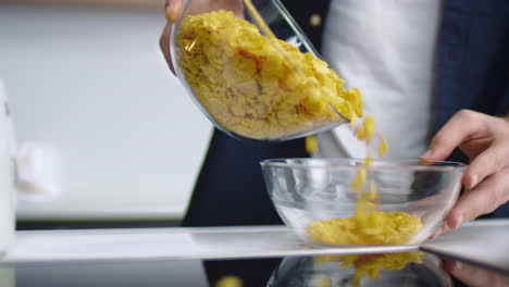 close up view of man hands pouring corn flakes into glass bowl