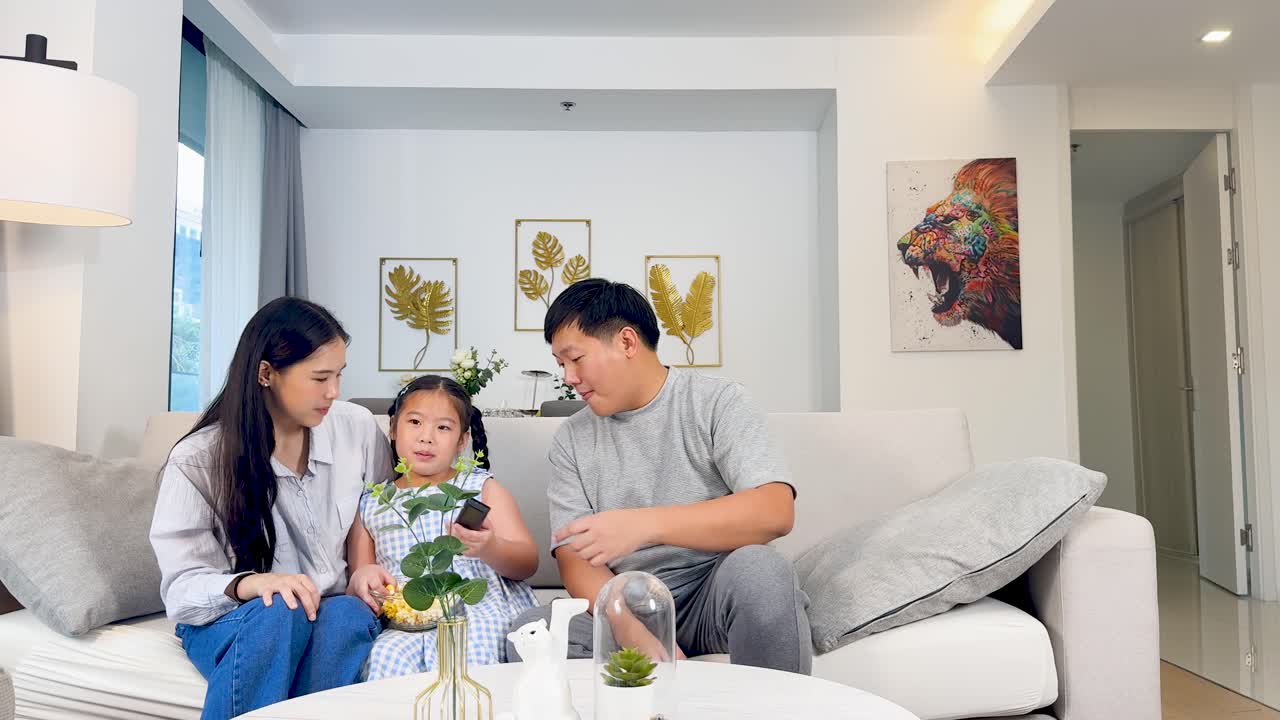 A family of three shares joyful moments on a cozy couch, enjoying snacks and laughter in a warmly lit living room