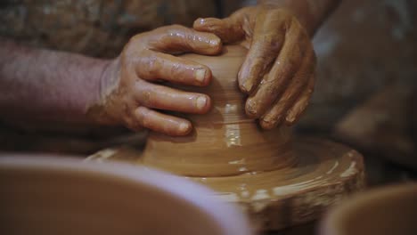 potter shaping a piece of red clay