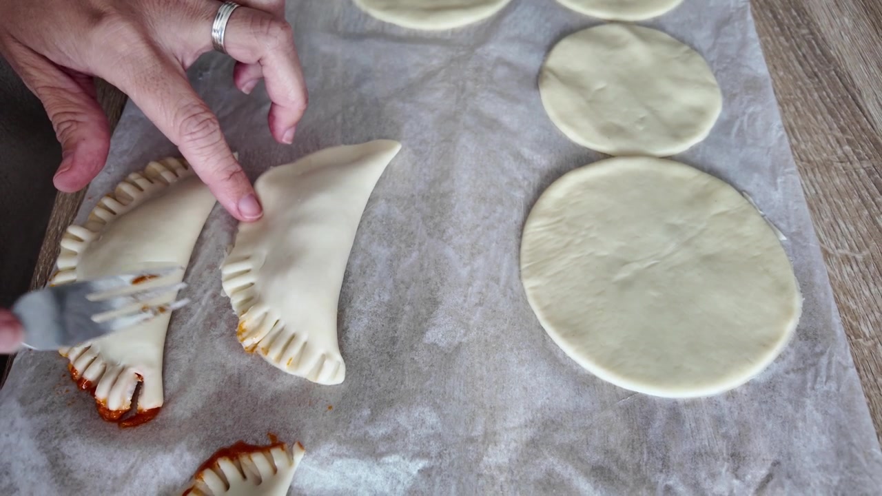Preparazione di empanadas al tonno a casa, mani che piegano la pasta, cucina casalinga tradizionale.