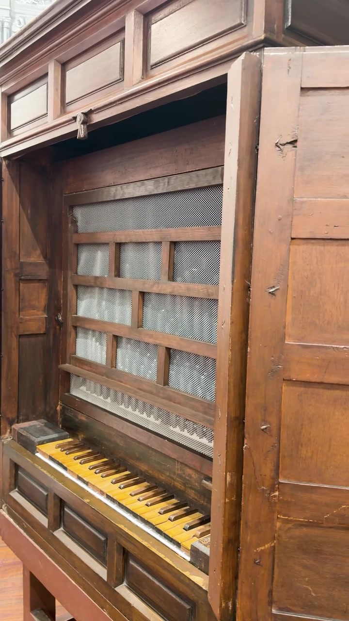 Pianoforte verticale antico con mobile in legno, tastiera a vista e dettagli interni decorativi, sfondo statico verticale ripreso a mano.