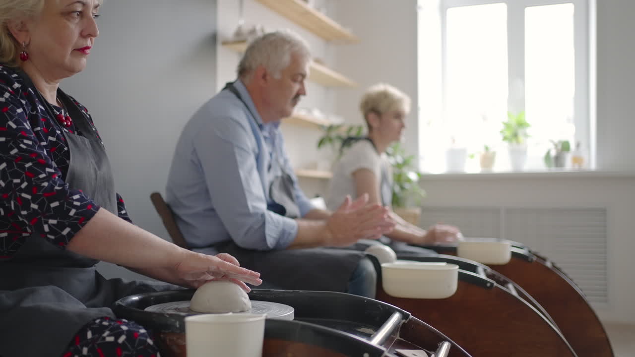 A group of senior women and a man together learn to make pottery on a potter's wheel. Making utensils on a retired potter's wheel