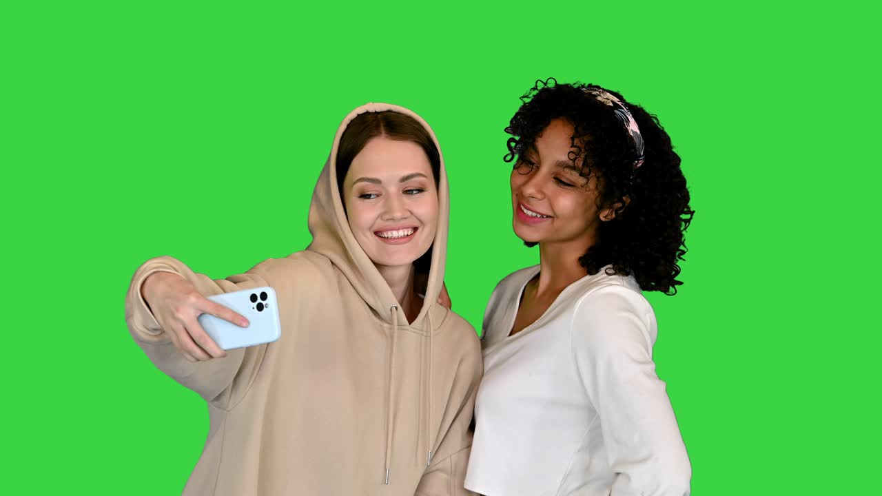 Two multicultural female friends posing and huggingtaking a selfie on a Green Screen, Chroma Key